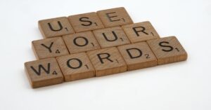 Letras de madeira dispostas dizendo 'USE YOUR WORDS' sobre fundo branco.