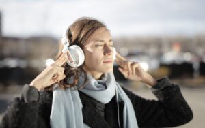 Como escolher a música ideal para viajar com estilo Mulher jovem de fones de ouvido brancos ouvindo música de olhos fechados ao ar livre