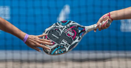 Beach Tennis: Fundamentos e Orientações para Iniciantes Duas mãos trocando uma raquete de esportes na quadra.