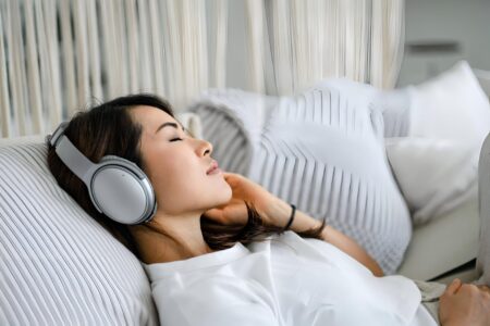 Jovem relaxando no sofá com fones de ouvido, olhos fechados.